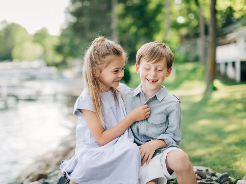 Young girl and boy laughing together by a lake