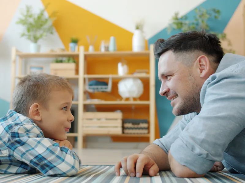 Man and a young boy lying on the floor, smiling at each other