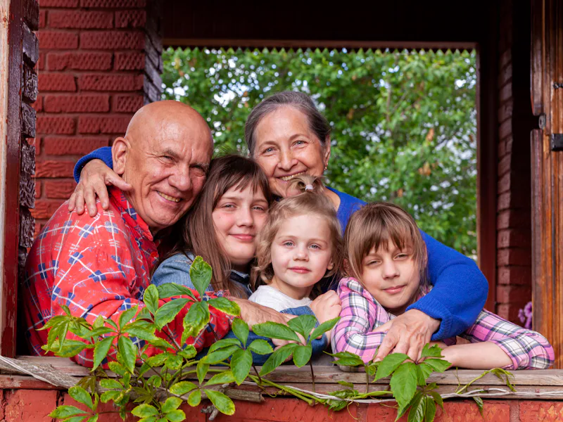 Two grandparents and three children hugging at a porch window