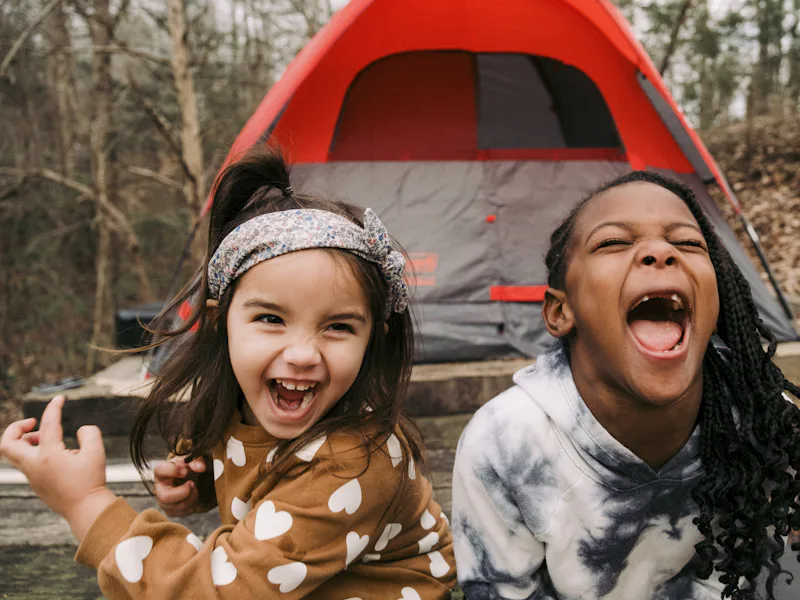 Two young girls laughing together outside a tent