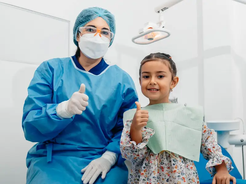 Young girl and her dentist both giving a thumbs up after a visit