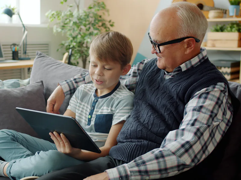 Older man and a boy looking at a tablet together on a couch