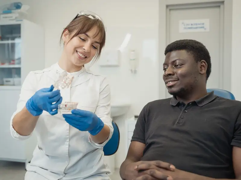 Smiling dental team member showing a model of teeth to a relaxed patient