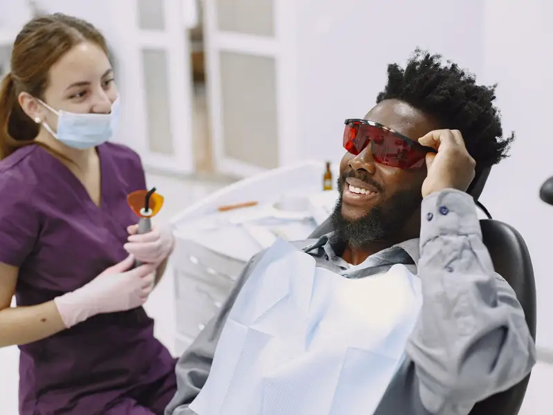 Man in tinted safety glasses laughing in a dental chair next to a hygienist