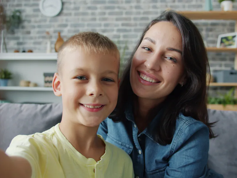 Woman and a young boy smiling for a selfie on a couch