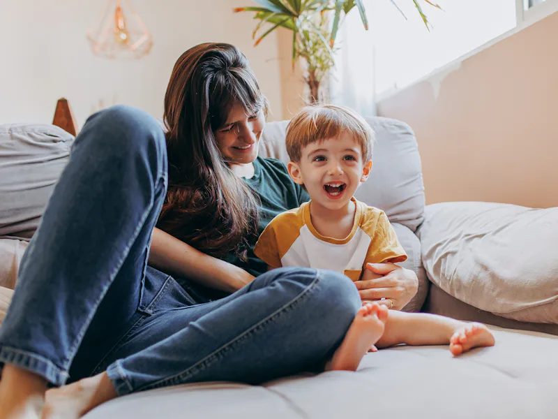 Woman and a laughing toddler relaxing on a couch
