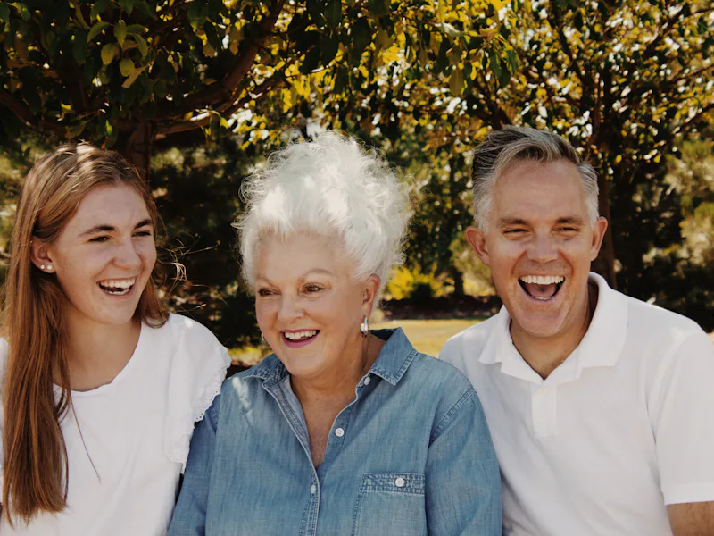 A young woman, an older woman and a man laughing together outdoors
