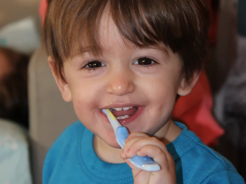 Smiling toddler brushing teeth with a blue toothbrush