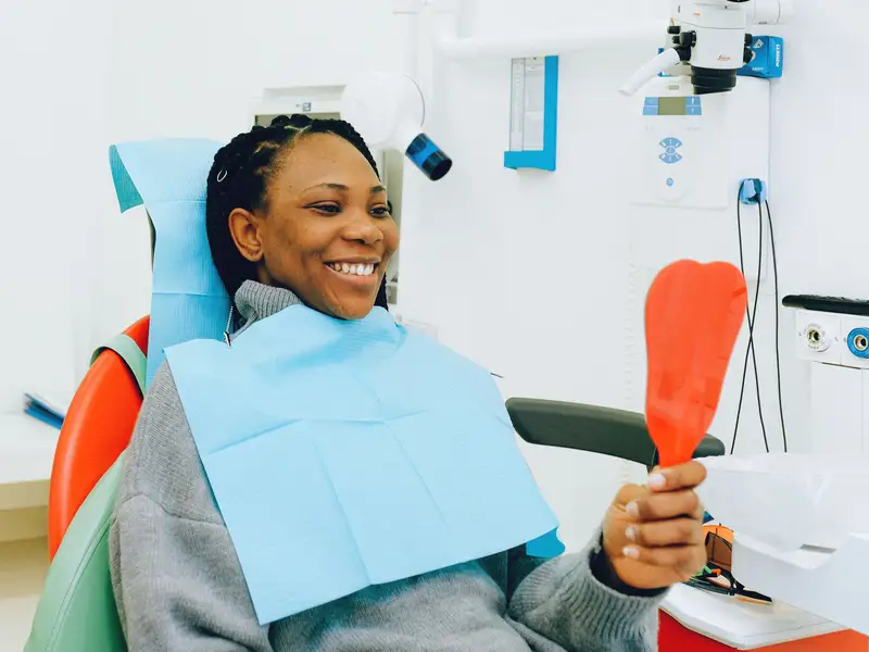 Woman in a dental chair smiling at her reflection in a hand mirror